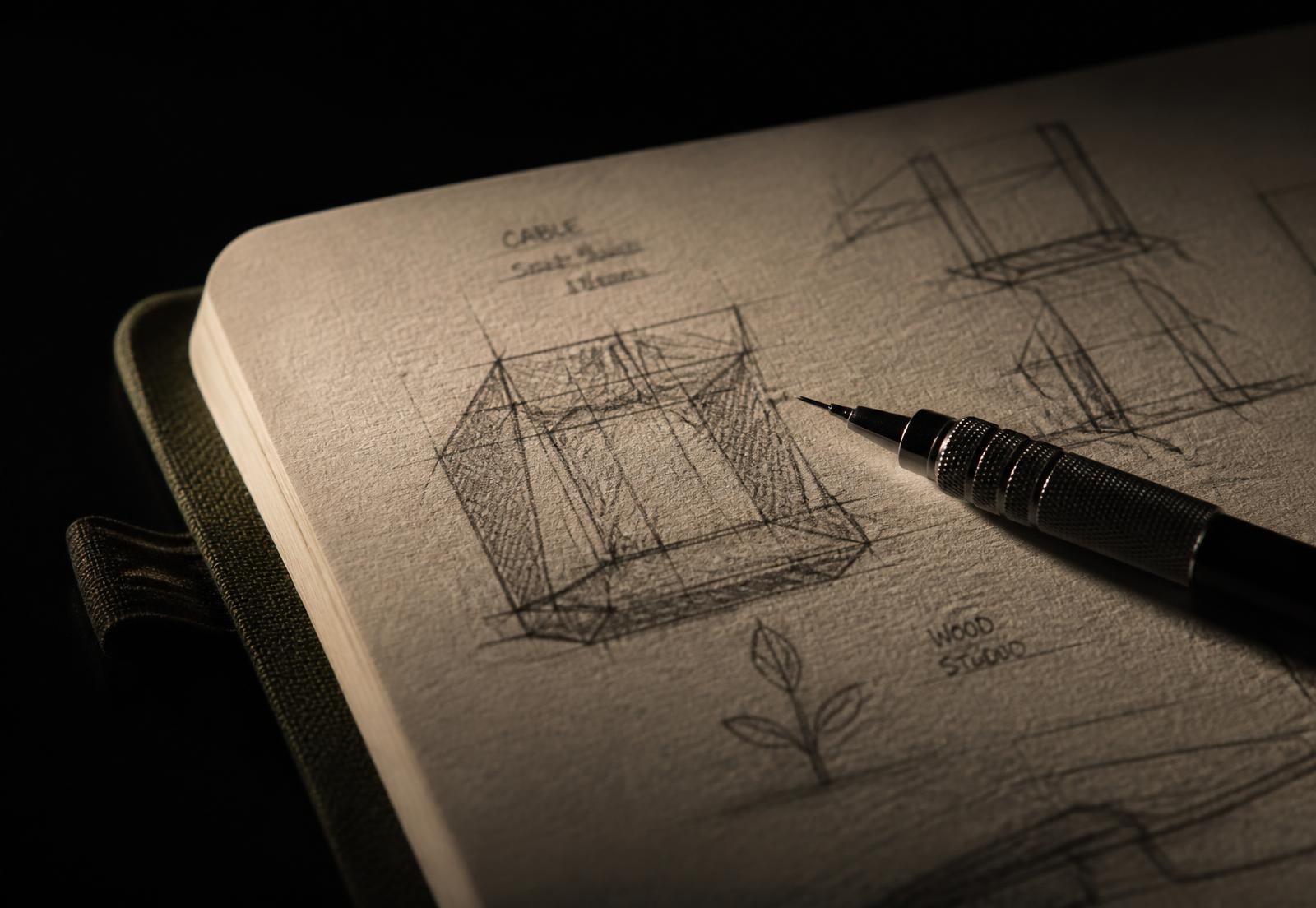 Pencil resting on fine wireframe sketches in a notebook, lit by a single warm light